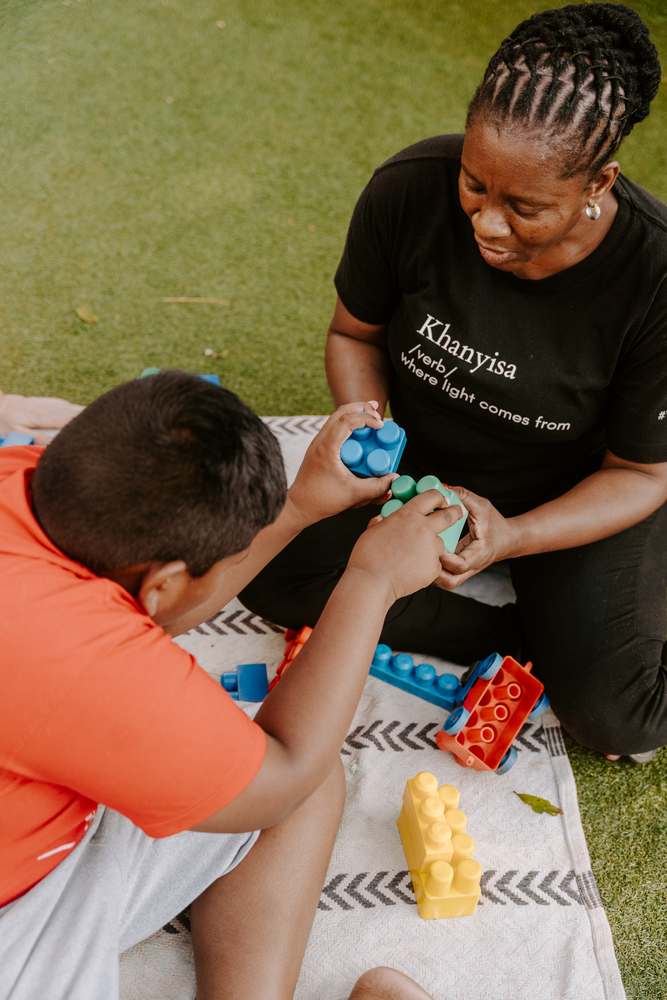 A Khanyisa specialist playing with building blocks alongside a child